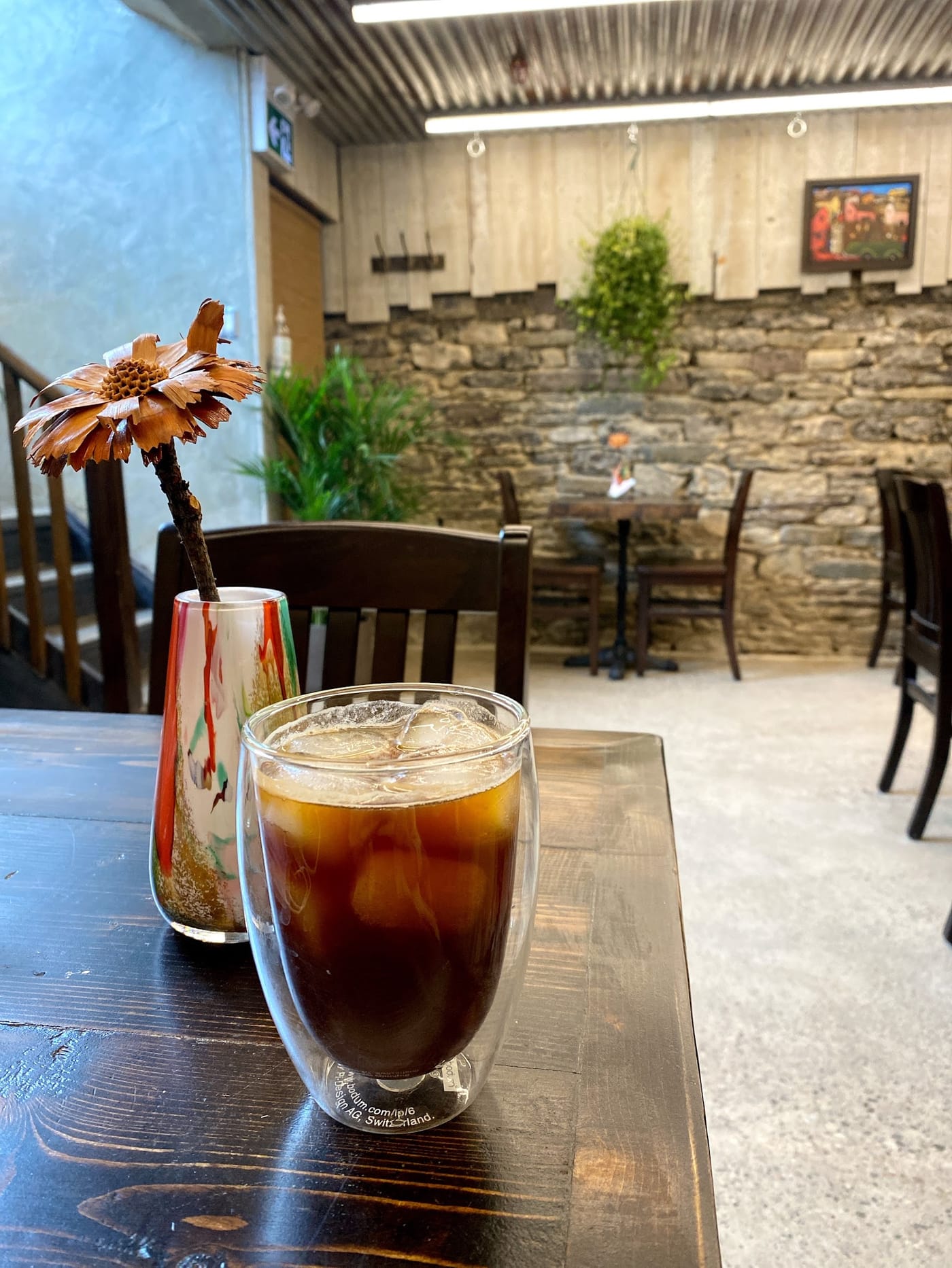An iced americano on a dark wood table against the stone wall